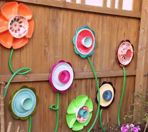 Make this DIY fence decor using supplies from the dollar store! Pick out various cups, bowls, plates and platters. Attach them together to create pretty flowers, then hang them on the fence. Use a green hose to make the stems. GREAT idea and easy to do!