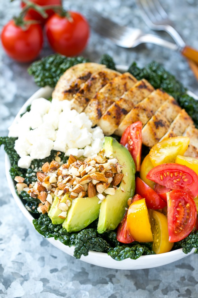 A bowl of Tuscan kale salad with grilled chicken, tomatoes, avocado and feta cheese.